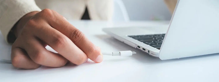 A person plugging in a charging cable to a laptop